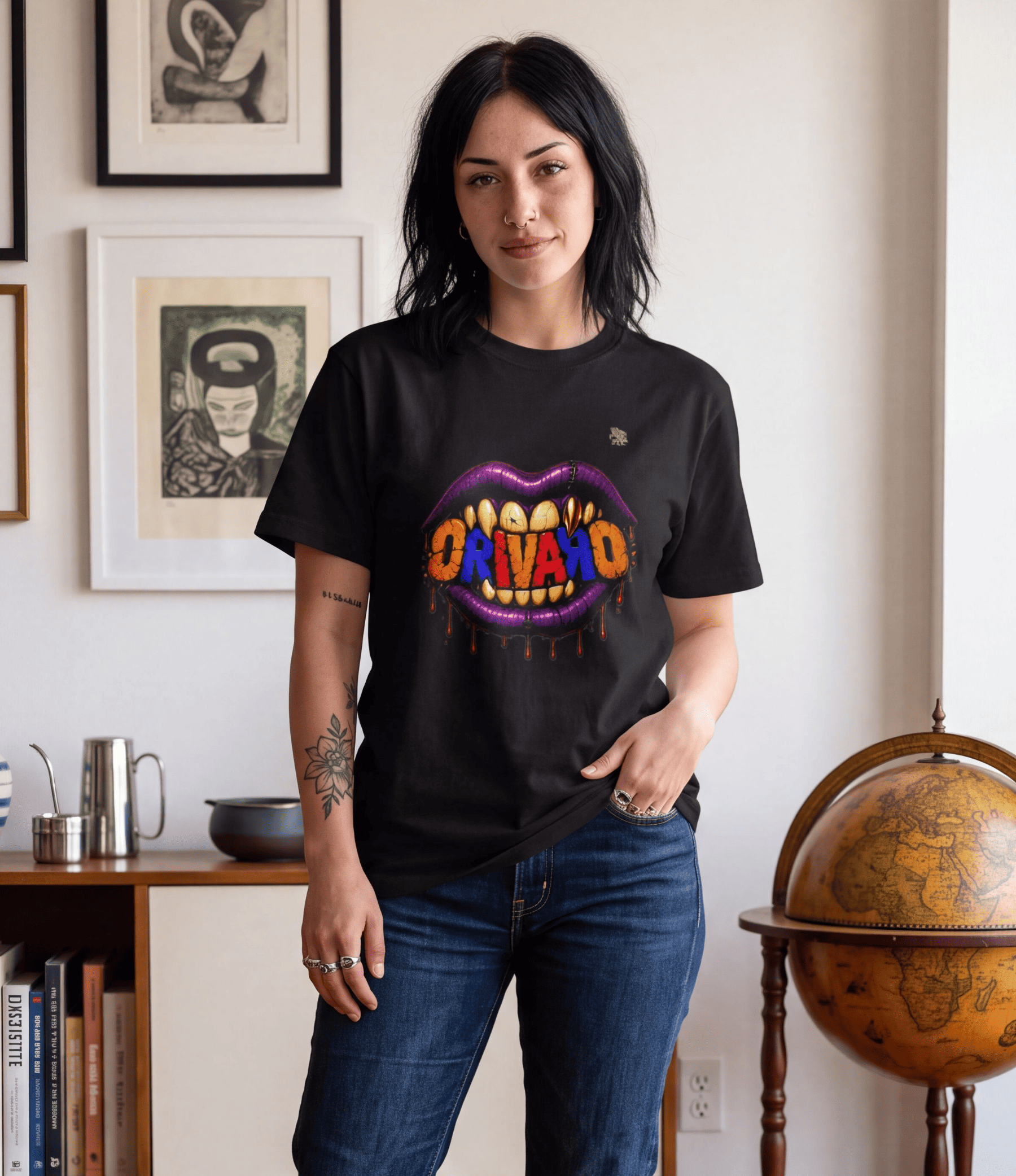 A woman wearing a black graphic t-shirt with a colourful 'ORIVARO' mouth design, paired with blue jeans, standing in a room with framed art and a globe in the background.