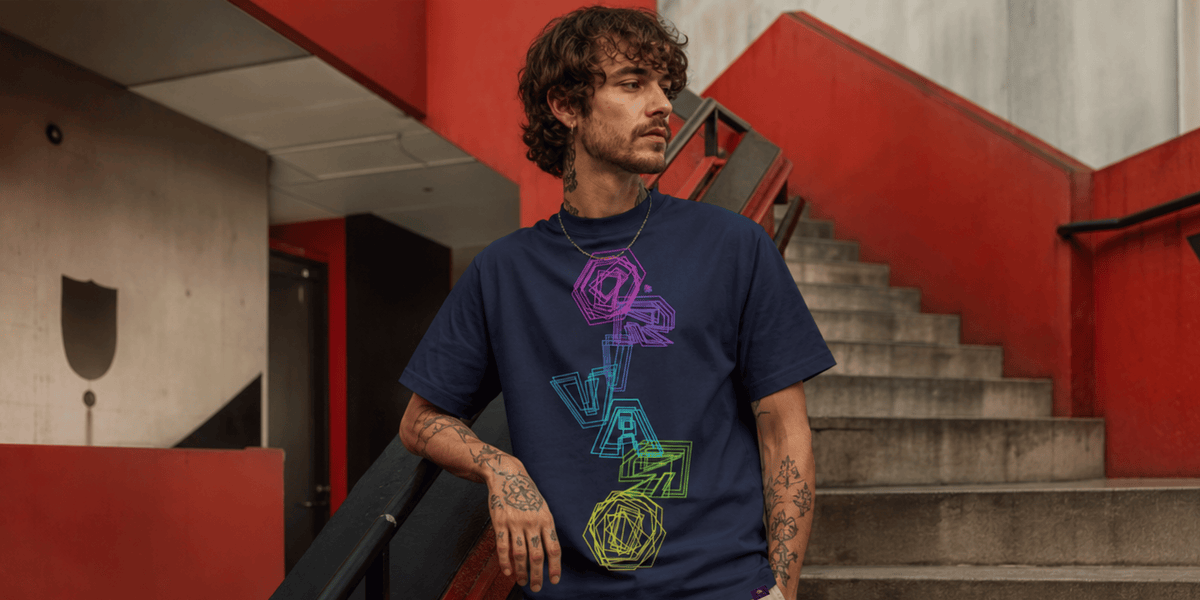 A man wearing a navy blue t-shirt with a colourful geometric graphic print, standing on concrete stairs in front of a red wall.