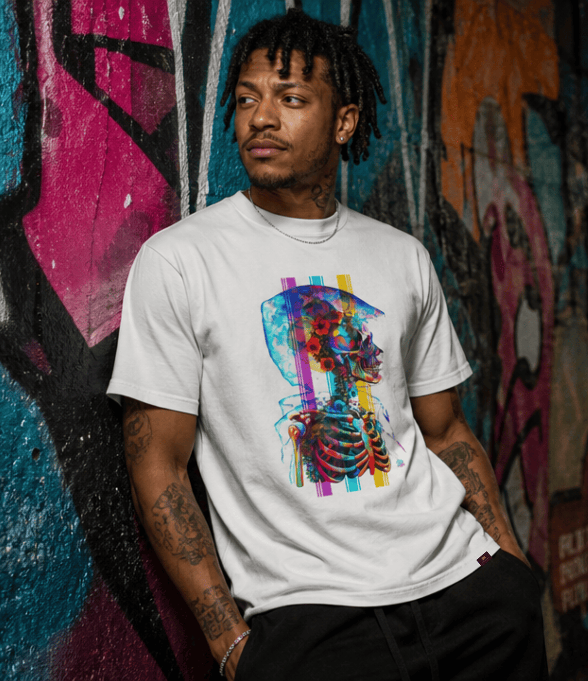 A man wearing a white crewneck t-shirt with a colourful graphic print of a stylized skull and rib cage, posed against a vibrant graffiti wall.