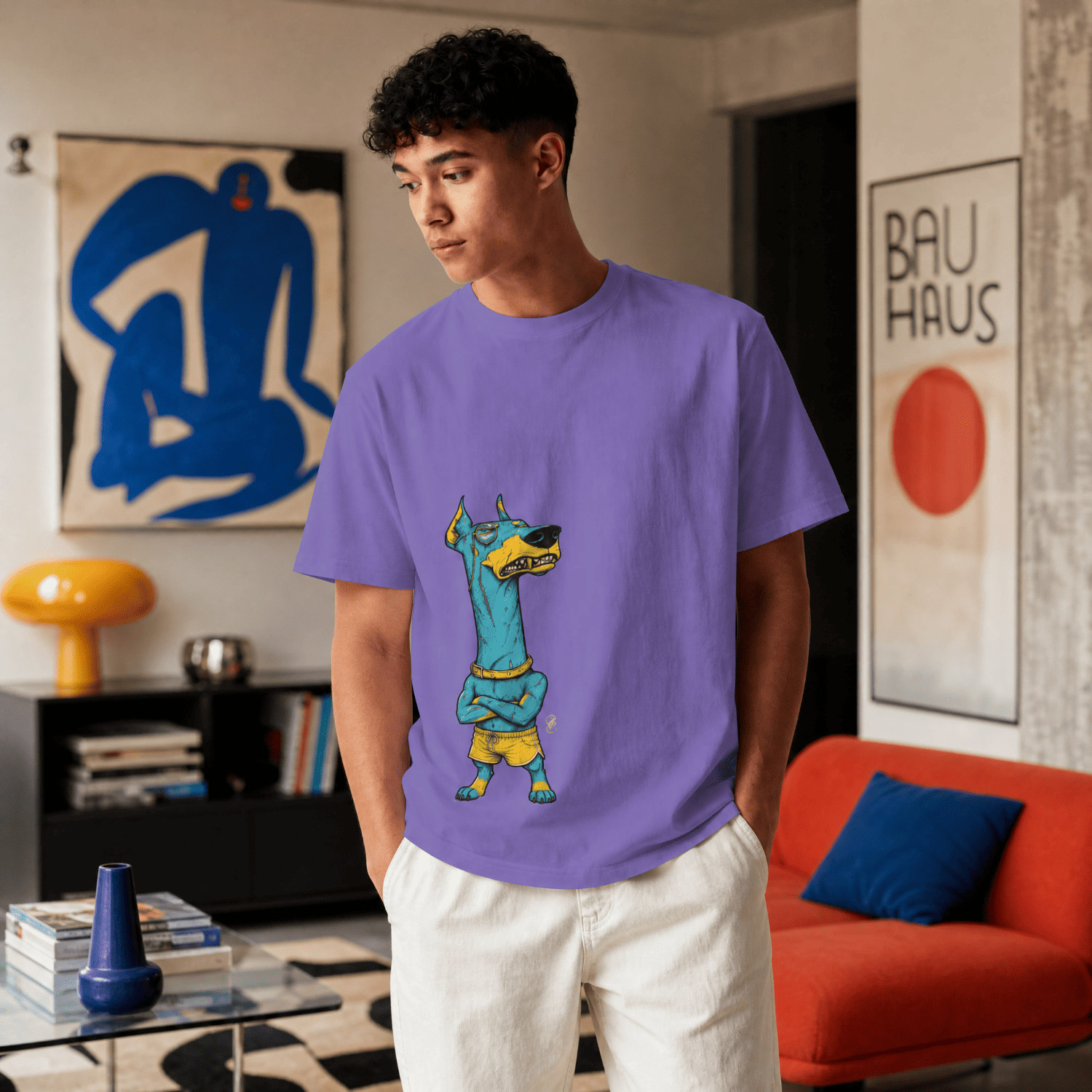 A man wearing a purple crewneck t-shirt with a cartoon graphic of a dog dressed in a soccer uniform, standing in a modern living room setting.