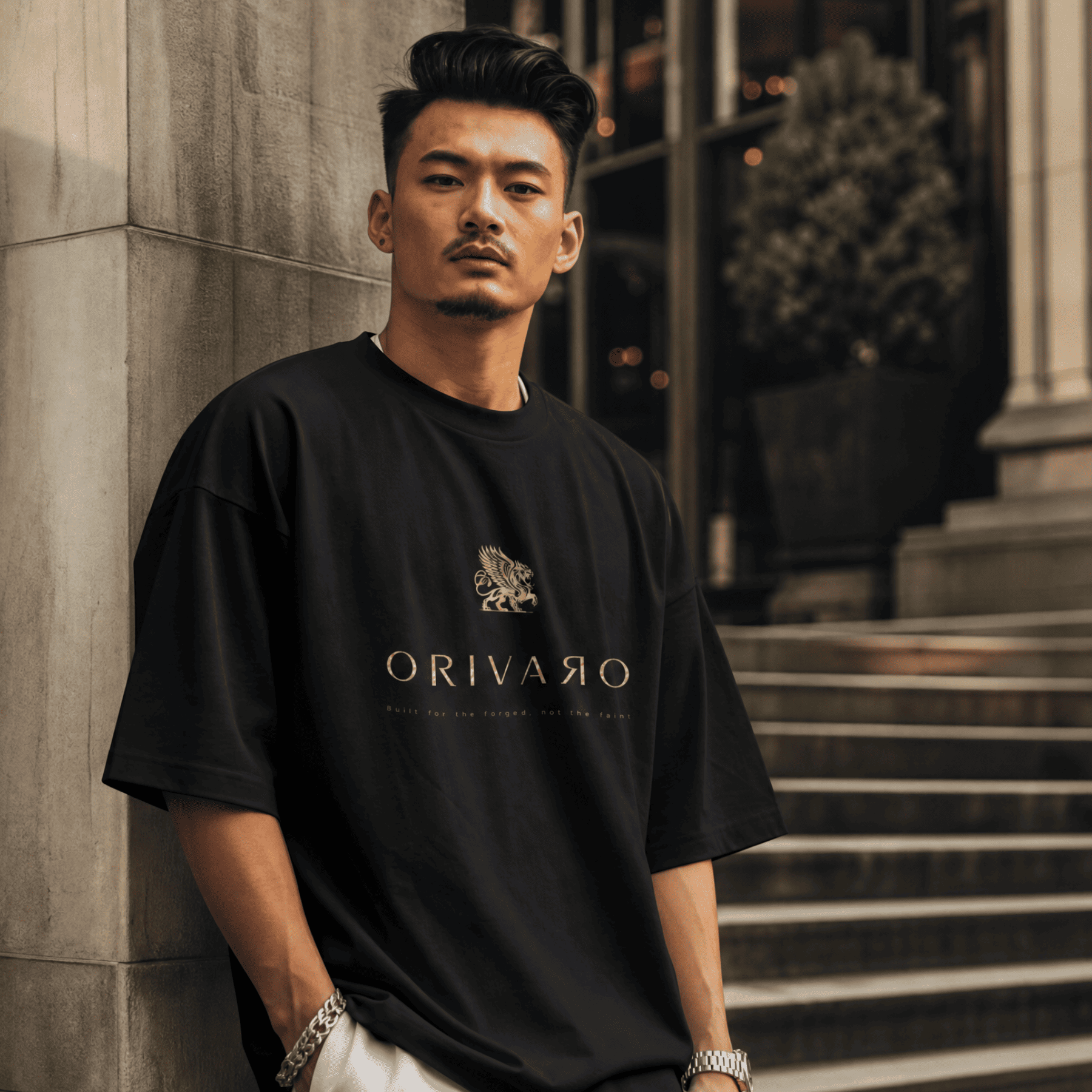 Man wearing a black 'Orivaro' t-shirt standing against a stone wall.