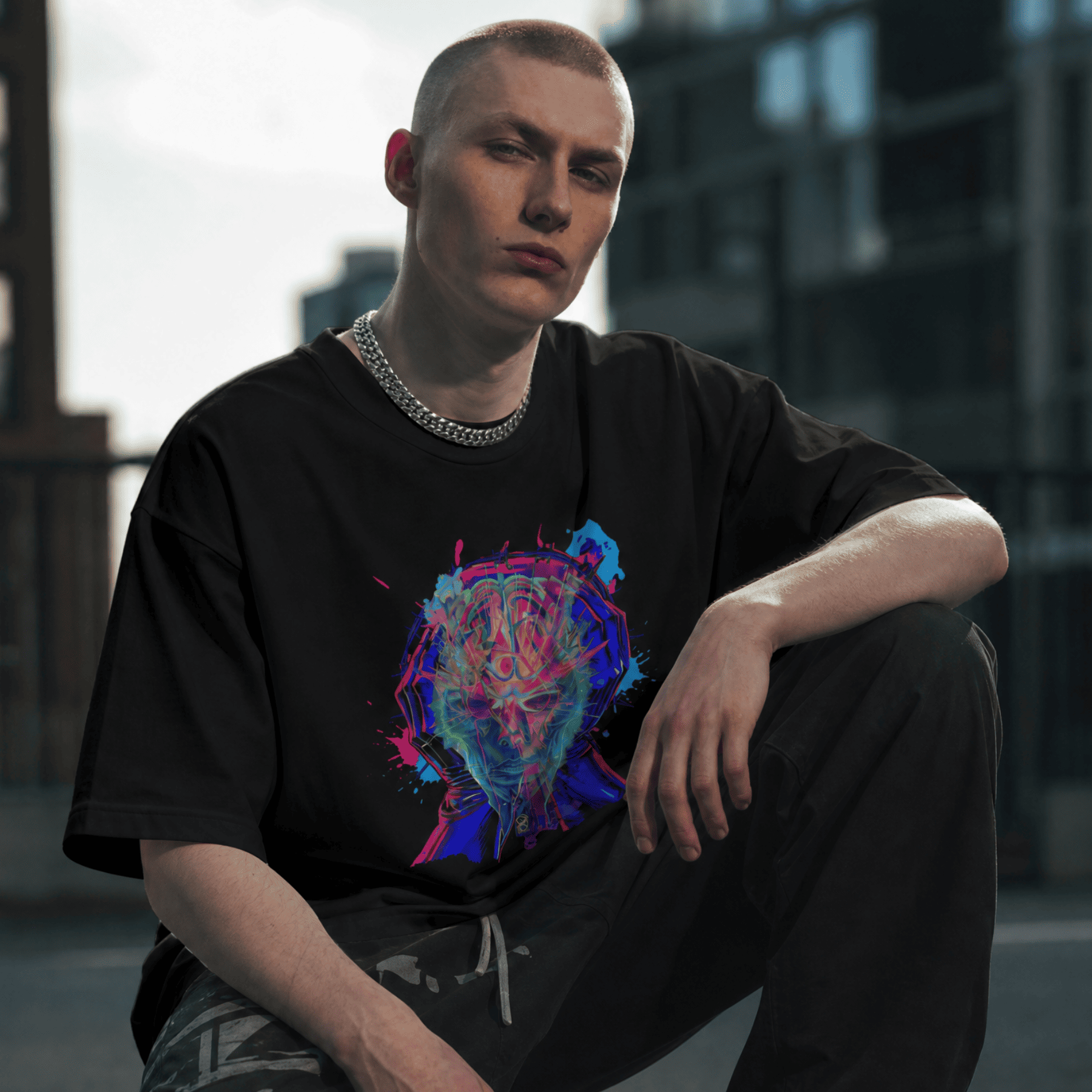 Person wearing a black t-shirt with a colorful graphic design, sitting in an urban setting.