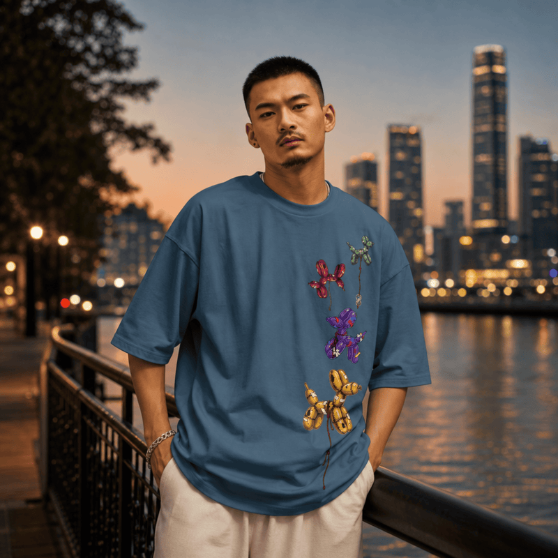 Man wearing a blue t-shirt with floral designs by a waterfront with city skyline in the background