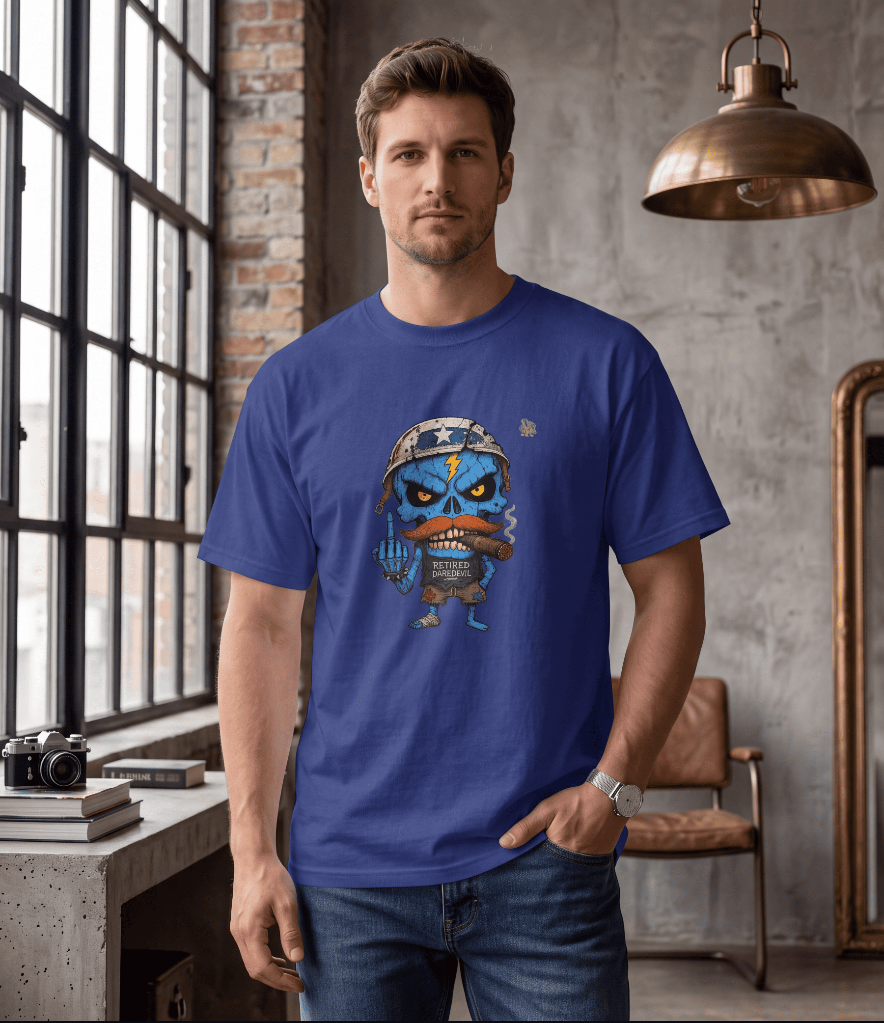 A man wearing a royal blue crewneck t-shirt with a cartoon graphic of a blue skull character with a mustache, standing in a loft-style room with a brick wall and window.