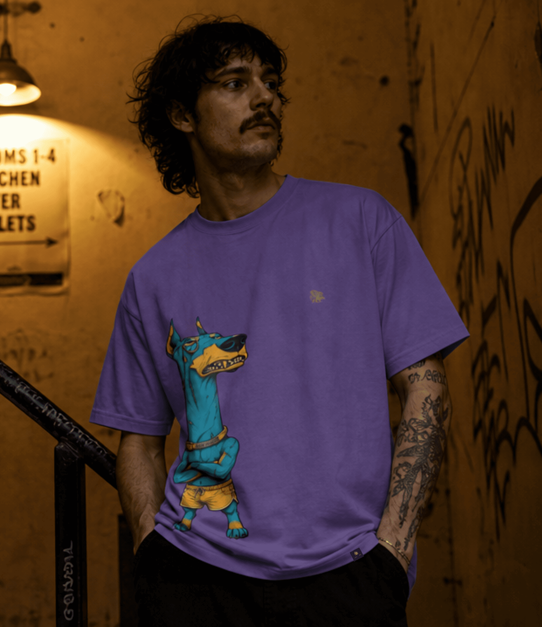 A man wearing a purple graphic t-shirt featuring a cartoon Doberman dog wearing a yellow 'MOTOTOWN' shirt, standing in a dimly lit alleyway.